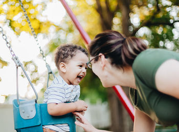 Young millennial mother and diverse mixed race toddler boy at park on nice summer day having fun