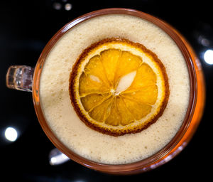 Top view of hot cappucino mug with dried lime slice on dark glassy surface