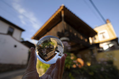 Cropped image of hand holding crystal ball against building