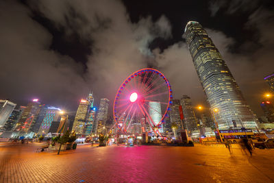 Illuminated ferris wheel against buildings at night