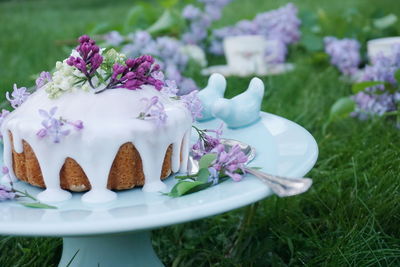Close-up of decorated cake with lilac flowers on stand at grassy field