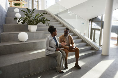 Businessman and businesswoman sitting on stair discussing in modern office