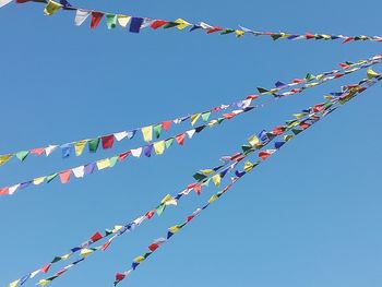 Low angle view of bunting hanging against clear blue sky