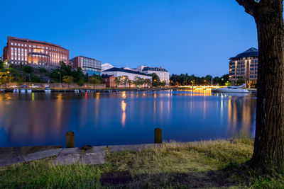 Illuminated buildings by lake against blue sky at dusk