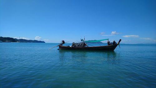 People on boat in sea against blue sky