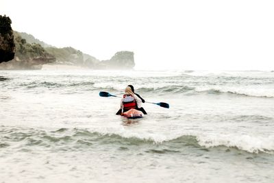 Rear view of people kayaking in sea against clear sky