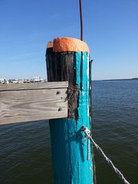 Close-up of wooden post by sea against clear blue sky