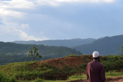 Rear view of man standing on field against sky