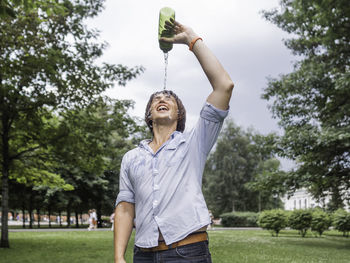 Smiling man pouring water on face at park