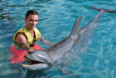High angle portrait of young man holding dolphin in sea