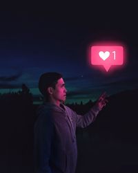 Man looking away while standing against illuminated wall at night