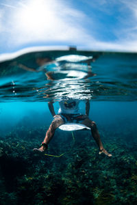 Underwater view of a surfer sitting on a surfboard in a clear sea