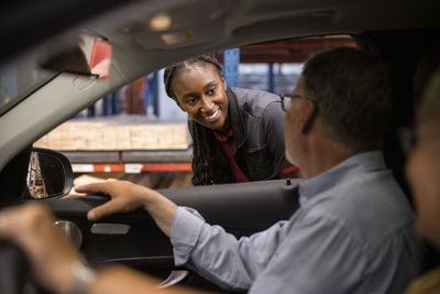 Smiling female sales staff looking at customer sitting in car at hardware store