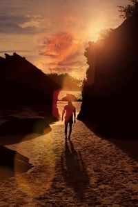 Rear view of man standing on sea shore against sky during sunset