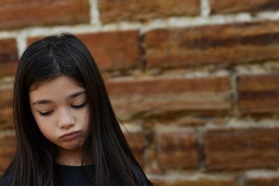 Close-up of sad girl against brick wall
