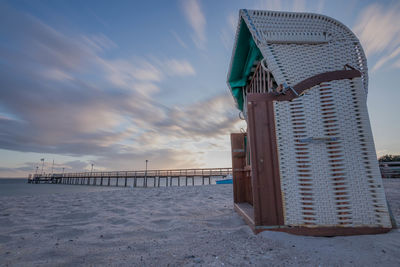 Hooded beach chairs on shore against sky during sunset