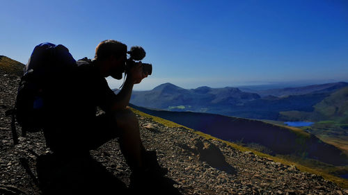 Man photographing on mountain against clear sky