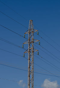 Low angle view of electricity pylon against blue sky