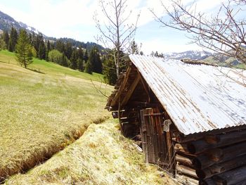 Wooden house on field by trees against sky