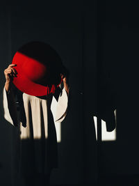 Midsection of woman holding hat while standing in darkroom