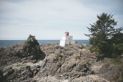 Lighthouse on rock by sea against sky