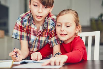 Siblings studying while sitting on chair at home