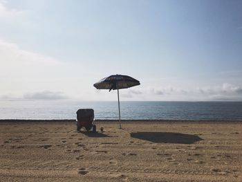 Parasol on sand at beach against sky