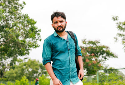 Portrait of young man standing against trees