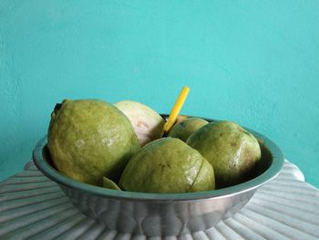 Close-up of fruits in bowl on table against wall