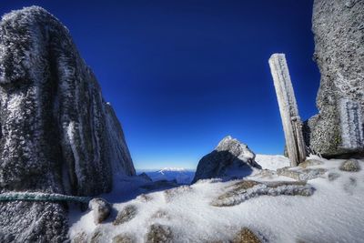 Icicles on rocks against clear blue sky during winter