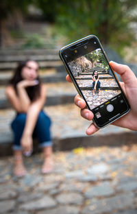 Cropped hand of person photographing woman sitting on staircase