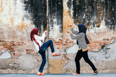 Full length of friends posing against weathered wall