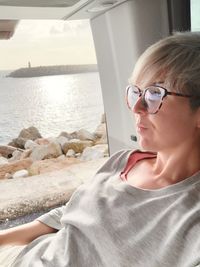 Woman looking away while relaxing by motor home window at beach