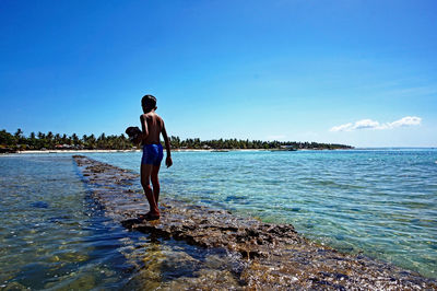 Rear view of man standing on beach against clear sky