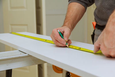 Midsection of man measuring wood in workshop