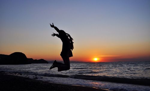 Silhouette man jumping at beach against clear sky during sunset