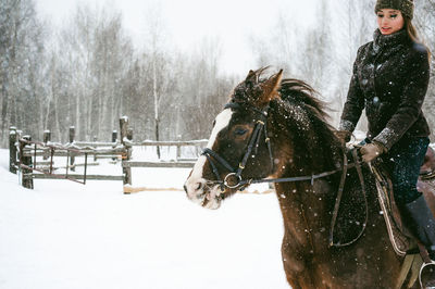 Beautiful woman riding horse on snow covered field