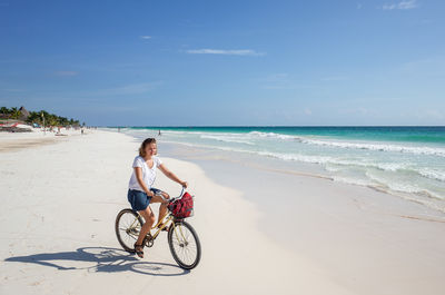 Woman riding bicycle on beach against sky