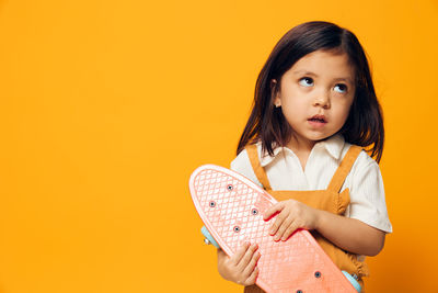 Cute girl holding skateboard against yellow background