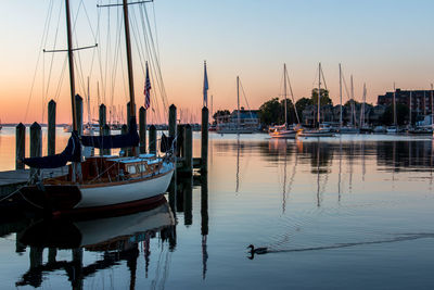 Sailboats moored in harbor at sunset