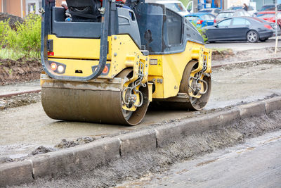 A yellow road roller tamping the foundation of a sidewalk at a construction site.