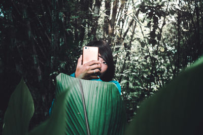 Woman photographing with smart phone in forest