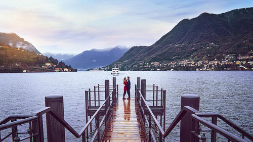 Side view of couple embracing pier on lake against sky