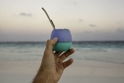 Close-up of hand holding sunglasses against sea at sunset