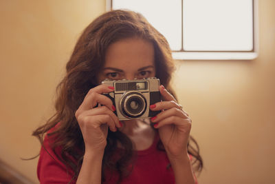 Portrait of woman photographing against yellow wall