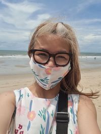 Portrait of young woman wearing sunglasses while sitting at beach