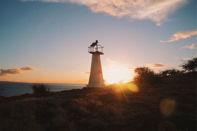 Silhouette lighthouse by sea against sky during sunset