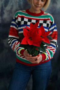 
a woman in a bright sweater holds a red poinsettia flower.
