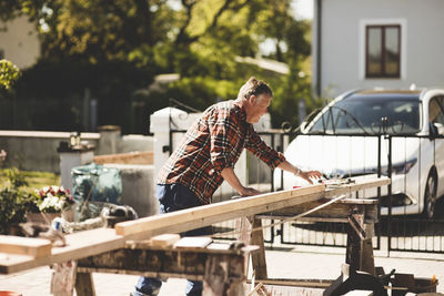 Side view of senior man measuring wooden plank at yard