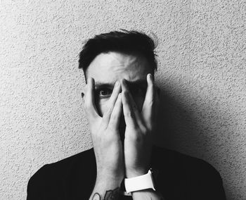 Portrait of young man covering face with hands while standing against wall